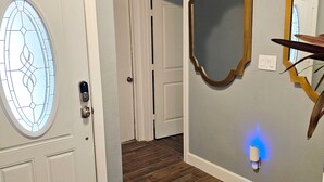 A hallway with wooden flooring, a white door with a stained glass window, and a wall-mounted mirror. - Mama’s Modern House is family and pet friendly, large yard, quartz countertops  (Cypress)