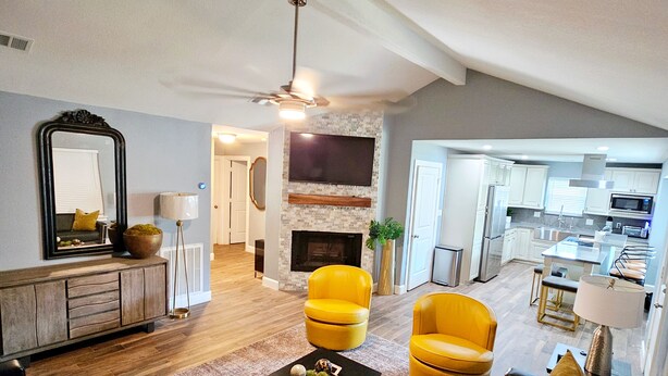 A modern living room with a fireplace, yellow armchairs, and a black sofa. - Mama’s Modern House is family and pet friendly, large yard, quartz countertops  (Cypress)
