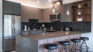 Uma cozinha moderna com ilha central, eletrodomésticos de aço inoxidável e banquetas de bar.