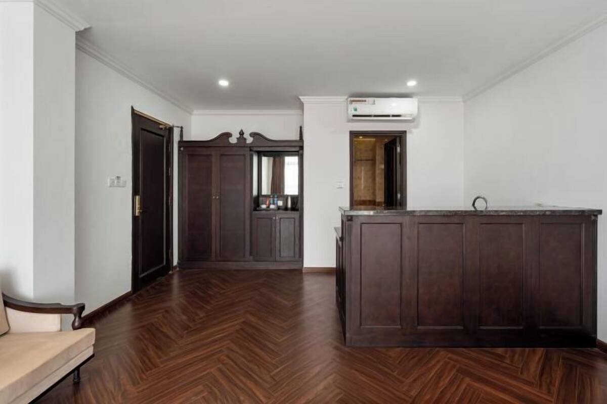 A spacious room with a herringbone wood floor, a dark wooden bench, and a kitchen area with a dark wooden counter and cabinets.
