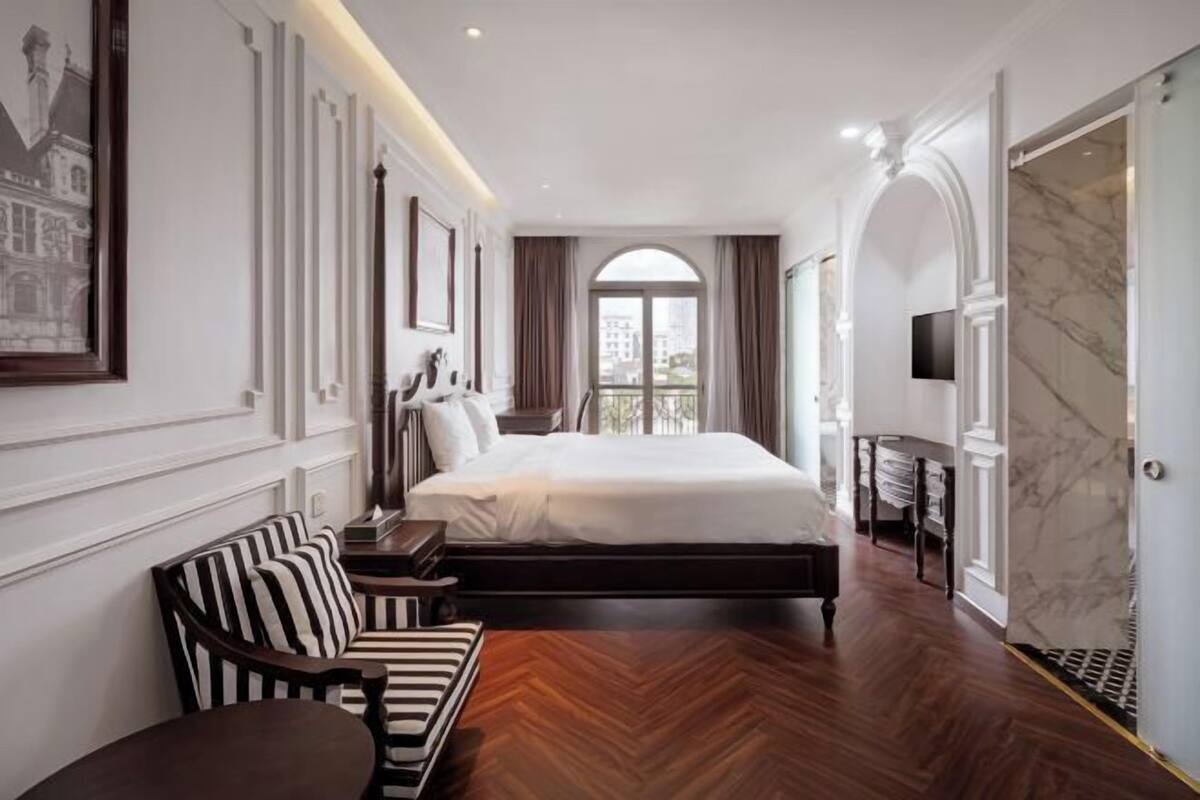A hotel room with a large bed, a sofa, a TV, and a view of the city.