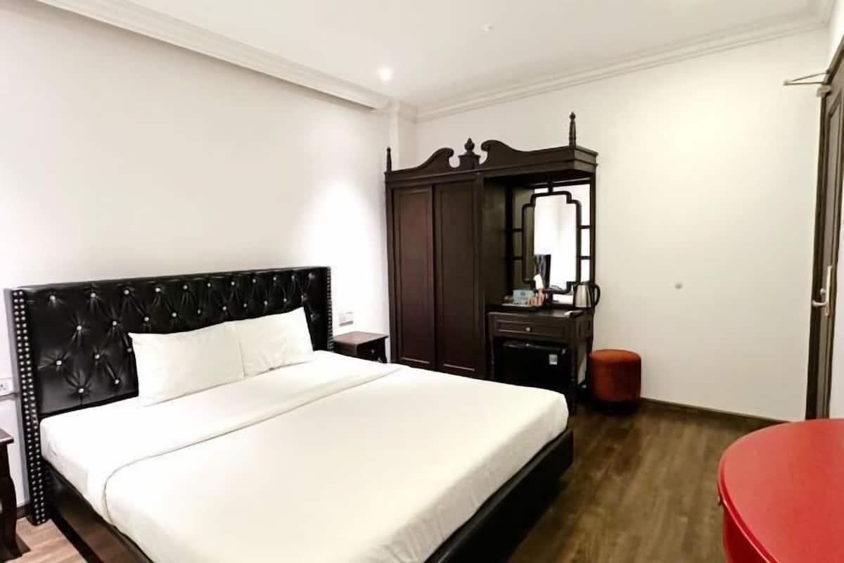 A hotel room with a bed, a wardrobe, a mirror, a red chair, and a small table.