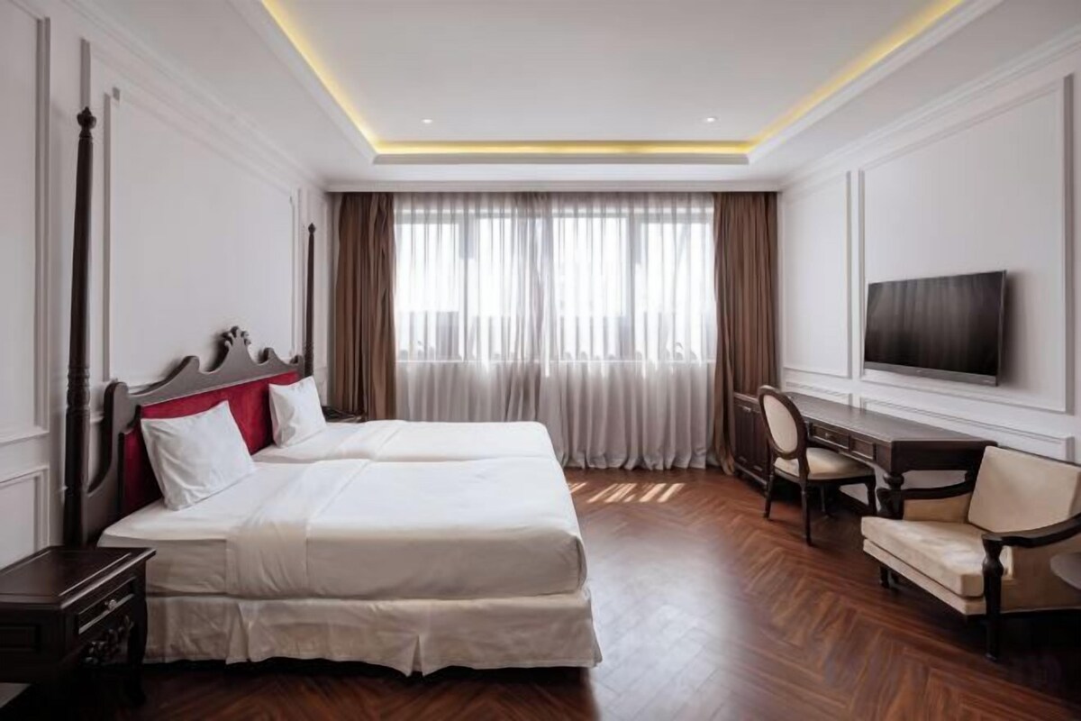 A hotel room with a large bed, a desk, a chair, and a television.