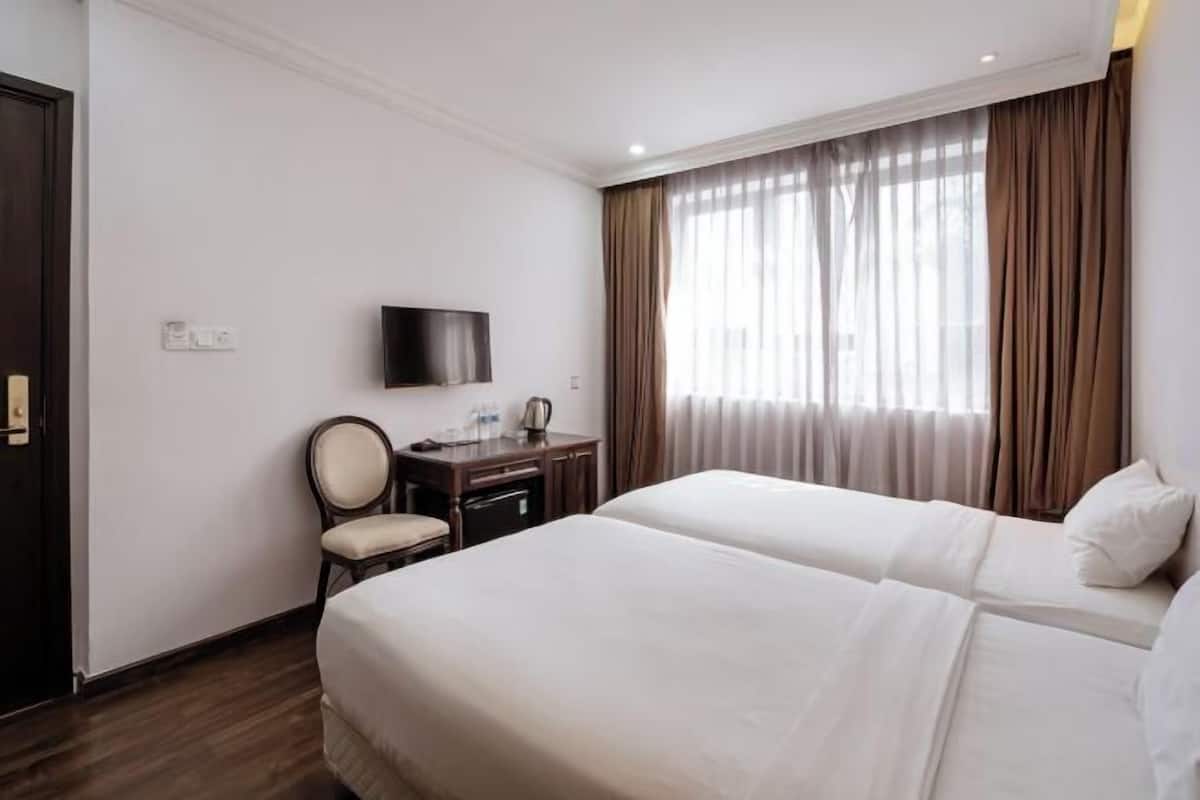 A hotel room with two beds, a desk, a chair, a TV, and a window with curtains.