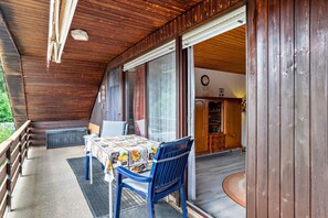 Een houten terras met een tafel, stoelen, een radiator en uitzicht op het interieur.