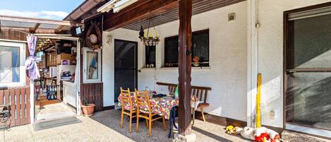 Un patio con una mesa, sillas, un banco de madera, una planta en maceta y un colgador de luz.