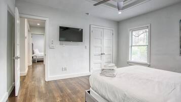 A bedroom with a bed, a ceiling fan, a TV, a door, and a window.