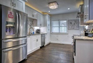 A modern kitchen with stainless steel appliances, white cabinetry, and a large window with blinds. - Buckhead Chateau Message Now for Summer Special (Atlanta)