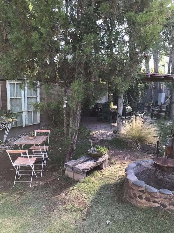 Un jardin avec une table et des chaises en bois, un bac à fleurs en pierre et un foyer.