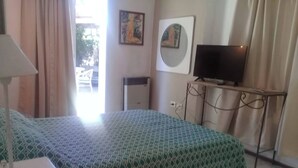 Ein Hotelzimmer mit Bett, Fernseher auf einem Schrank, Schreibtisch mit Lampe und einem Fenster mit Vorhängen.