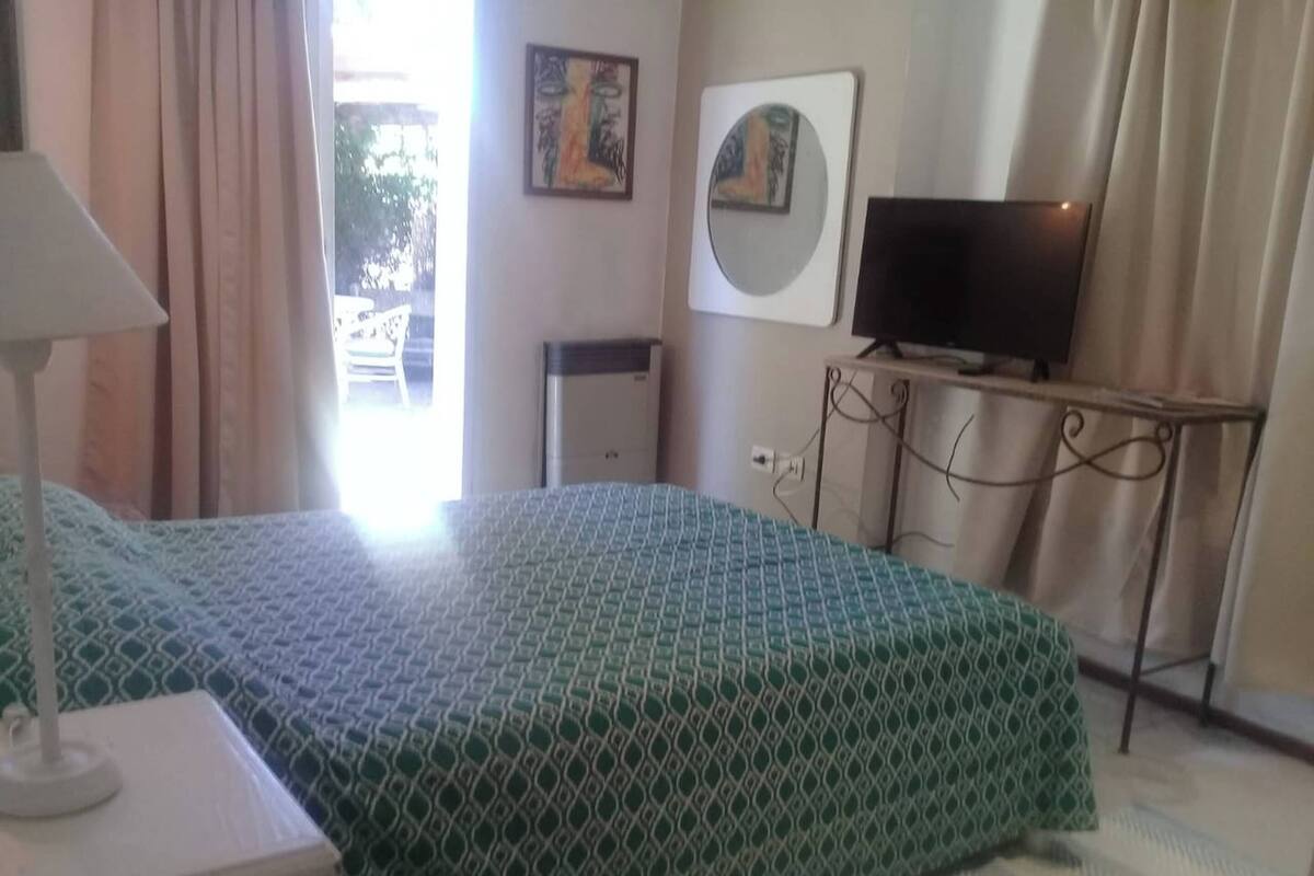 Ein Hotelzimmer mit Bett, Fernseher auf einem Schrank, Schreibtisch mit Lampe und einem Fenster mit Vorhängen.