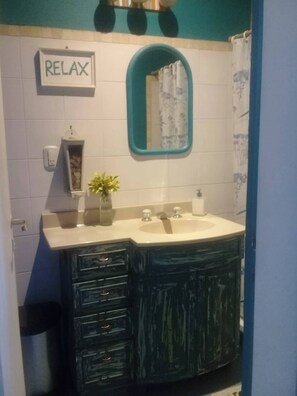 Une salle de bain avec un lavabo blanc, un miroir avec un cadre turquoise, un panneau indiquant « RELAX », une petite étagère avec une plante et un rideau de douche bleu.