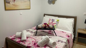 A neatly made bed with a floral bedspread, a tray with toiletries, and a painting of two white doves on the wall. - Zebrano Apartment in Kallithea Rhodes (Rhodes)