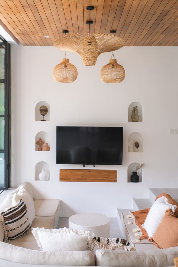 Una sala de estar moderna con un televisor de pantalla plana grande montado en una pared de madera, rodeada de sofás blancos y una mesa de centro redonda.