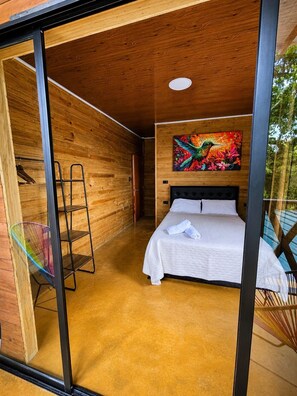 Une chambre à coucher avec un lit, une échelle, un tableau et une porte vitrée donnant sur un espace extérieur.