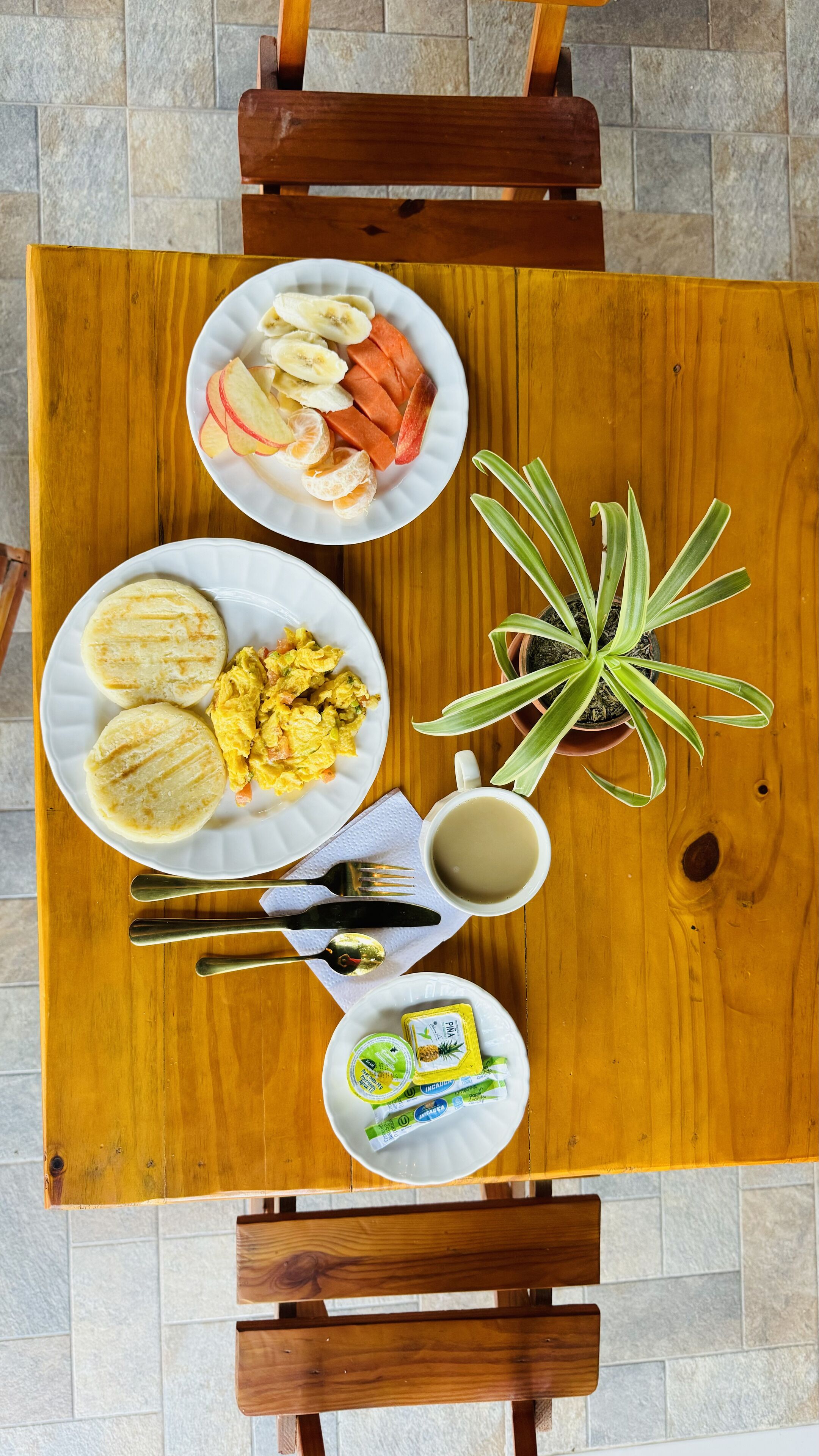 Une table de salle à manger en bois, avec des assiettes remplies de nourriture, une plante et une tasse.