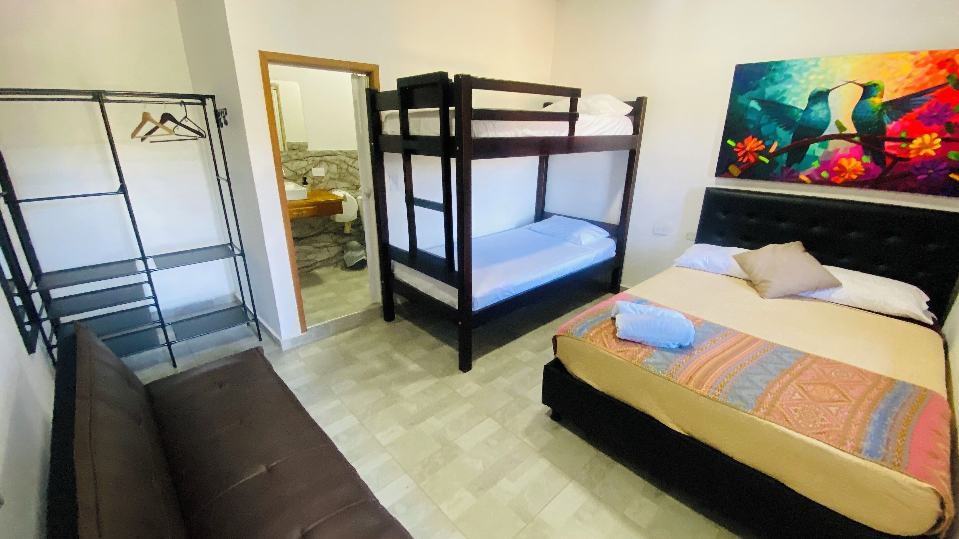 Une pièce comprenant un lit superposé, un canapé, une armoire et une salle de bain visible à travers une porte ouverte.