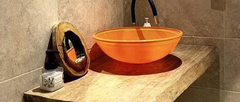 A bathroom with a wooden vanity, an orange sink, a round mirror, and a towel ring.