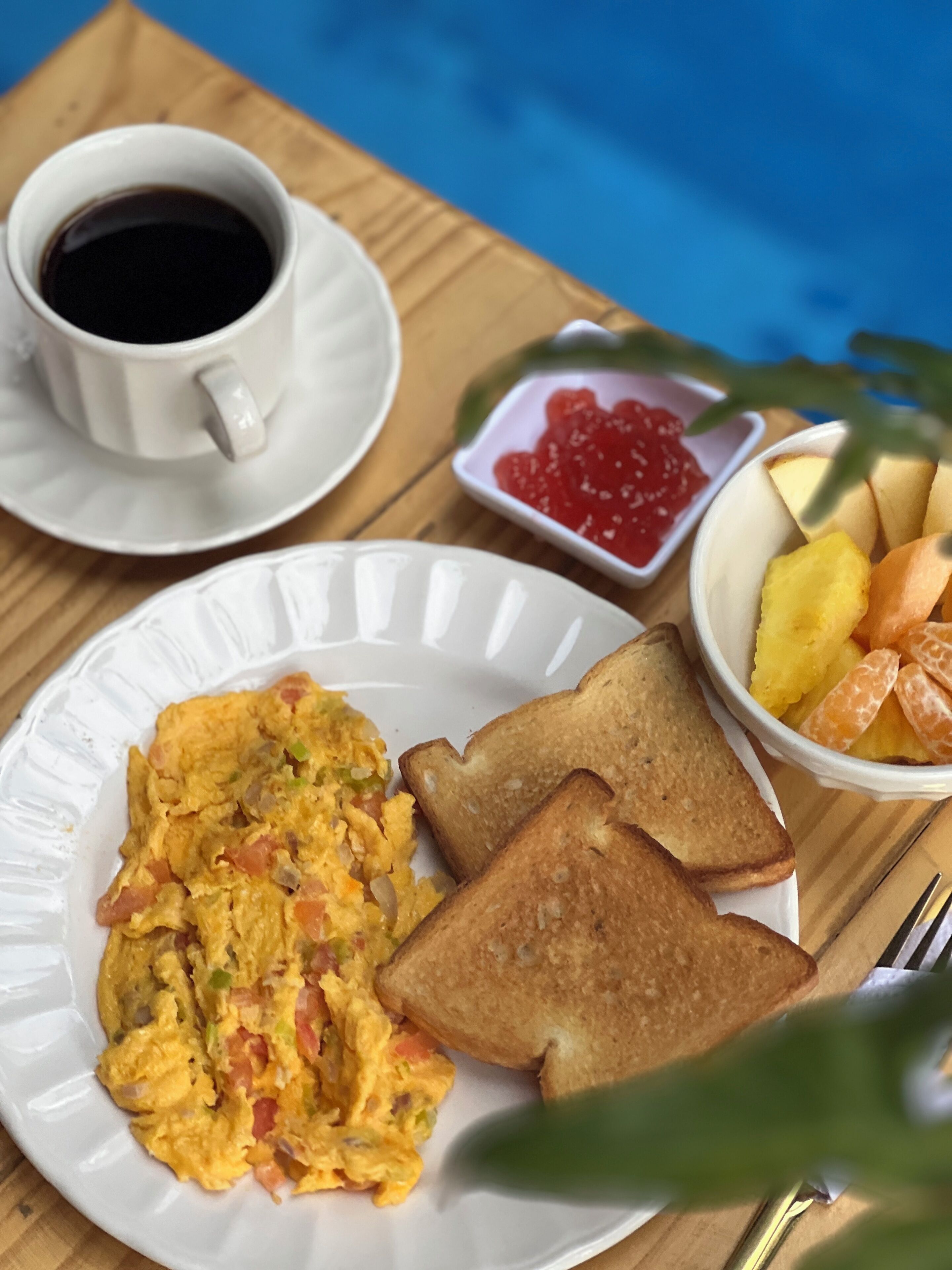 Un plato de desayuno con huevos revueltos, tostadas y un bol de fruta.