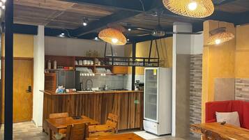 Ein Restaurant mit Holztischen und -stühlen, einer Küche und hängenden Korbstühlen.