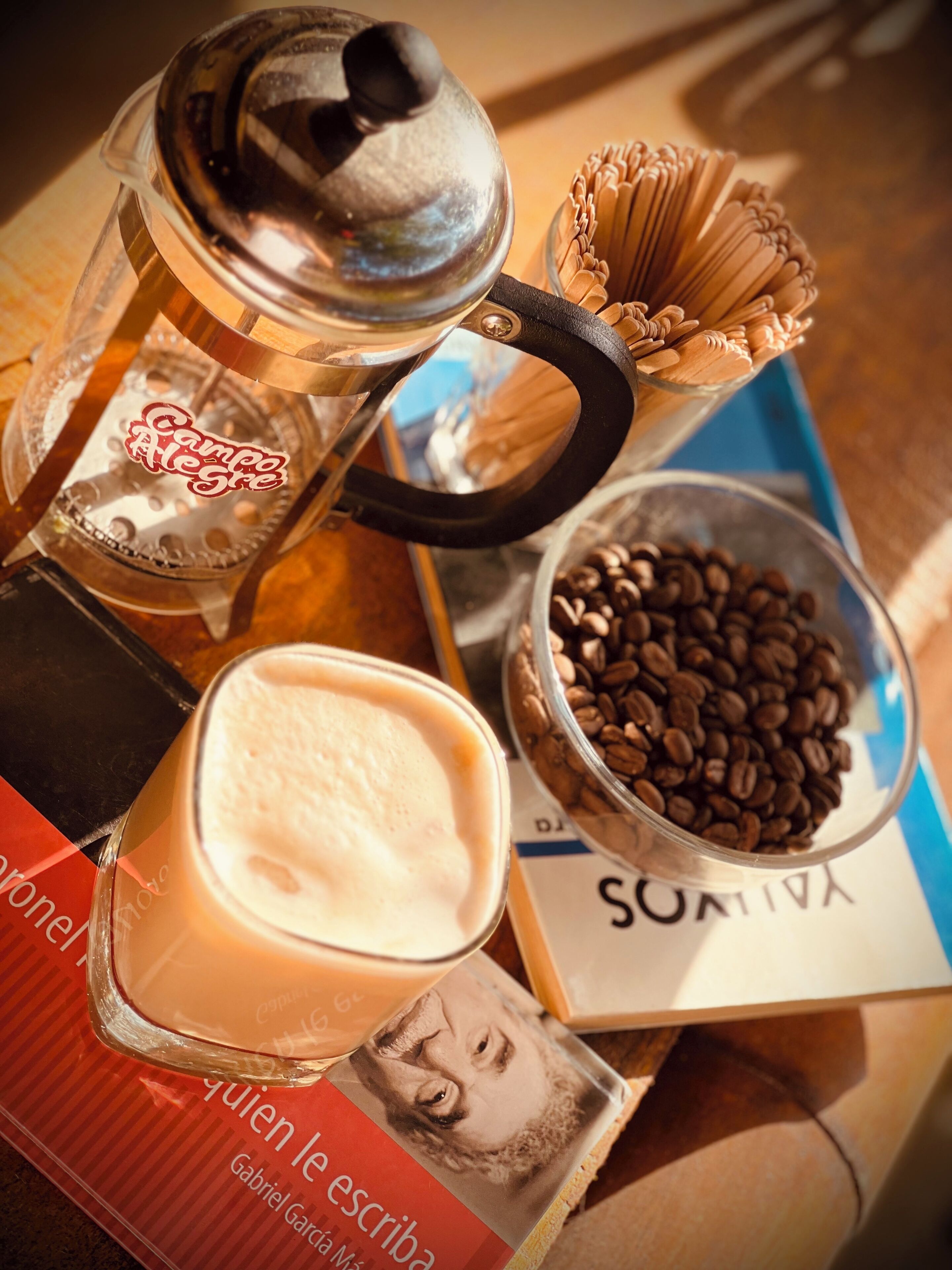 A coffee maker, a glass of coffee, a bowl of coffee beans, and a book titled "Gabriel Garcia Marquez".