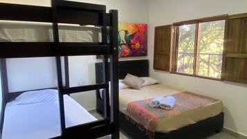 A room with a bunk bed, a single bed, a colorful painting, and a window with a view of trees.