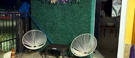 An outdoor seating area with two white chairs and a neon sign that reads 'Coffee House Minca.'