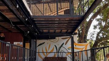A swimming pool with a tiled deck, surrounded by a metal fence and a covered area with a mural.