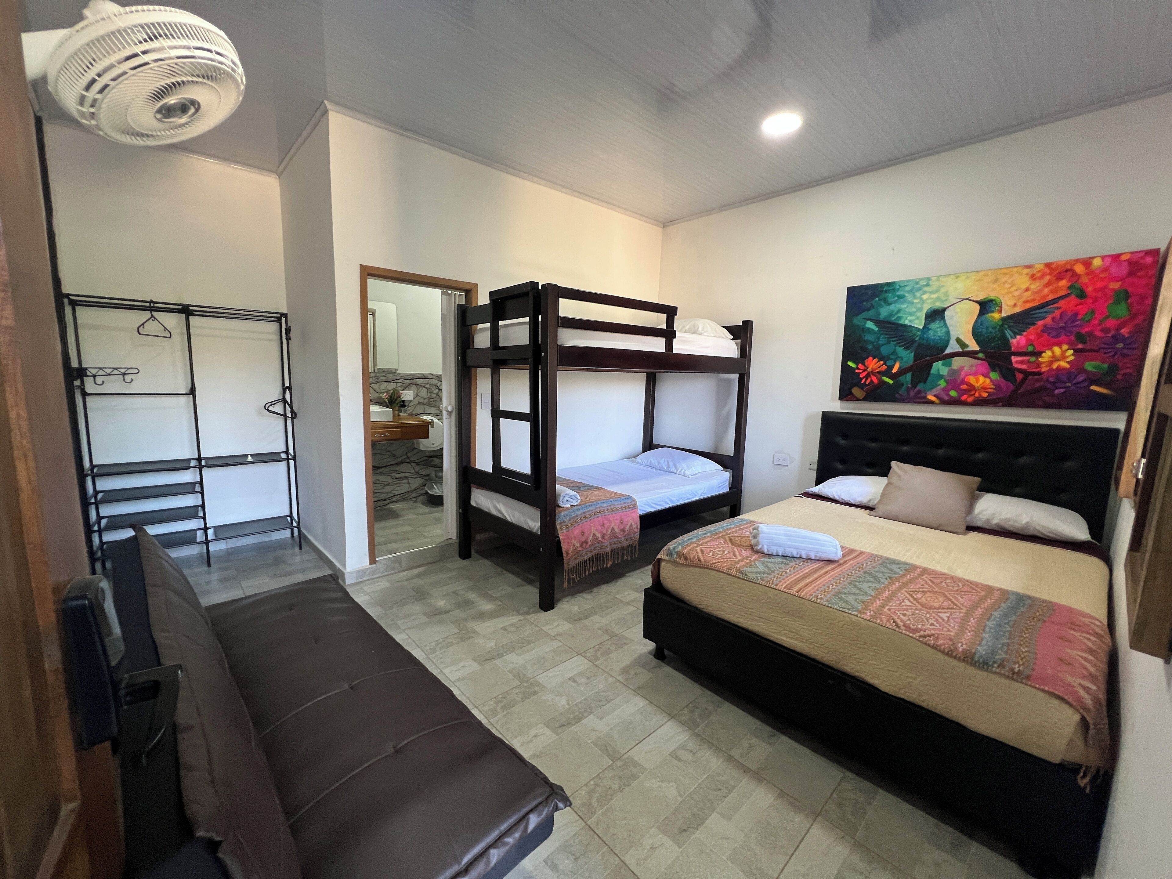 A bedroom with two bunk beds, a sofa, a painting, and a ceiling fan.