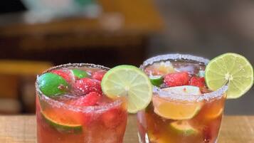 Dos vasos de una bebida roja con rodajas de lima y fruta sobre una mesa de madera.