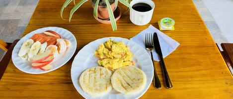 A wooden table with breakfast plates, a coffee cup, a plant, and a small container of yogurt.