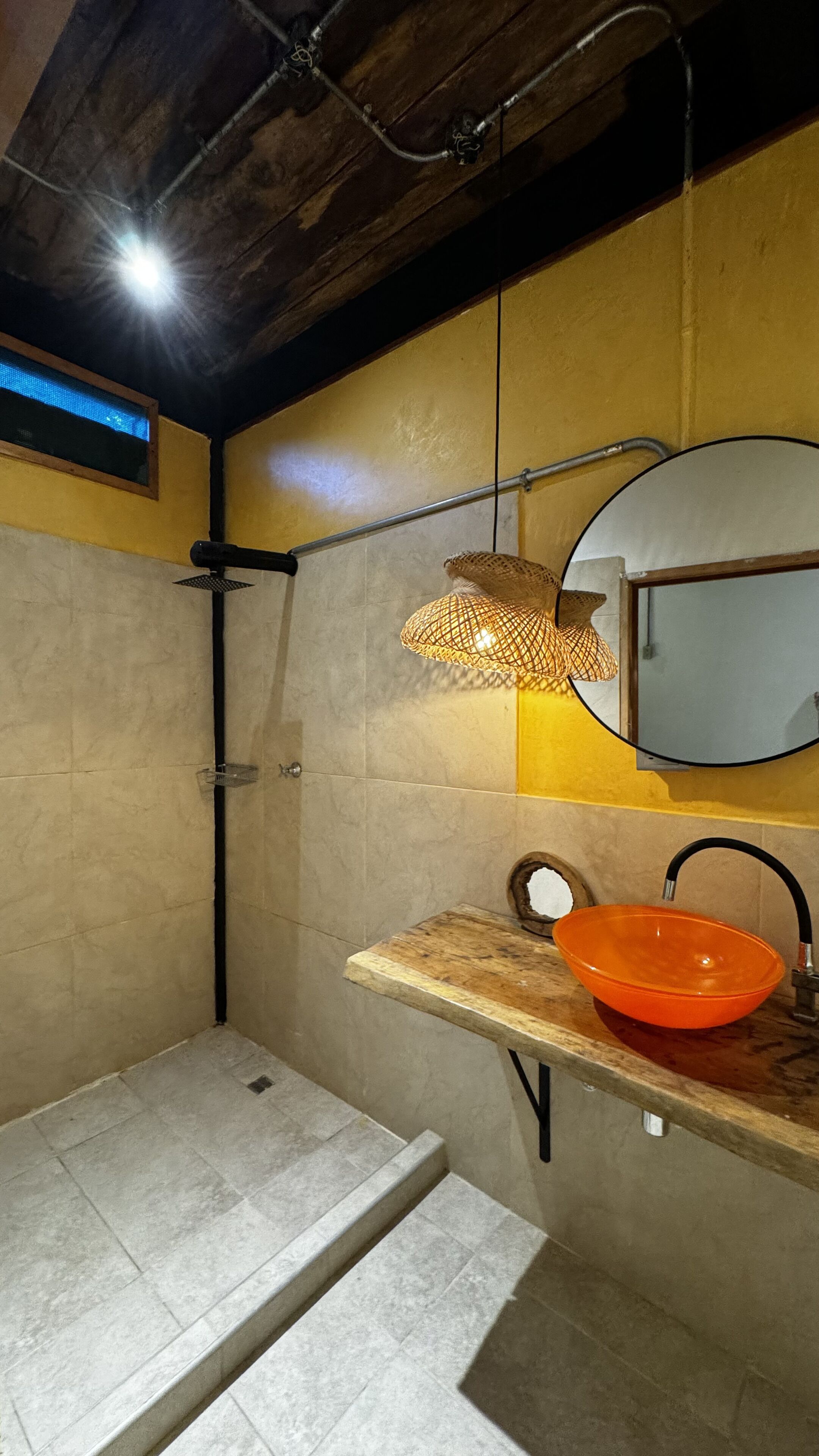 Un bagno con doccia, un lavabo con lavandino arancione, uno specchio e una lampada a sospensione.