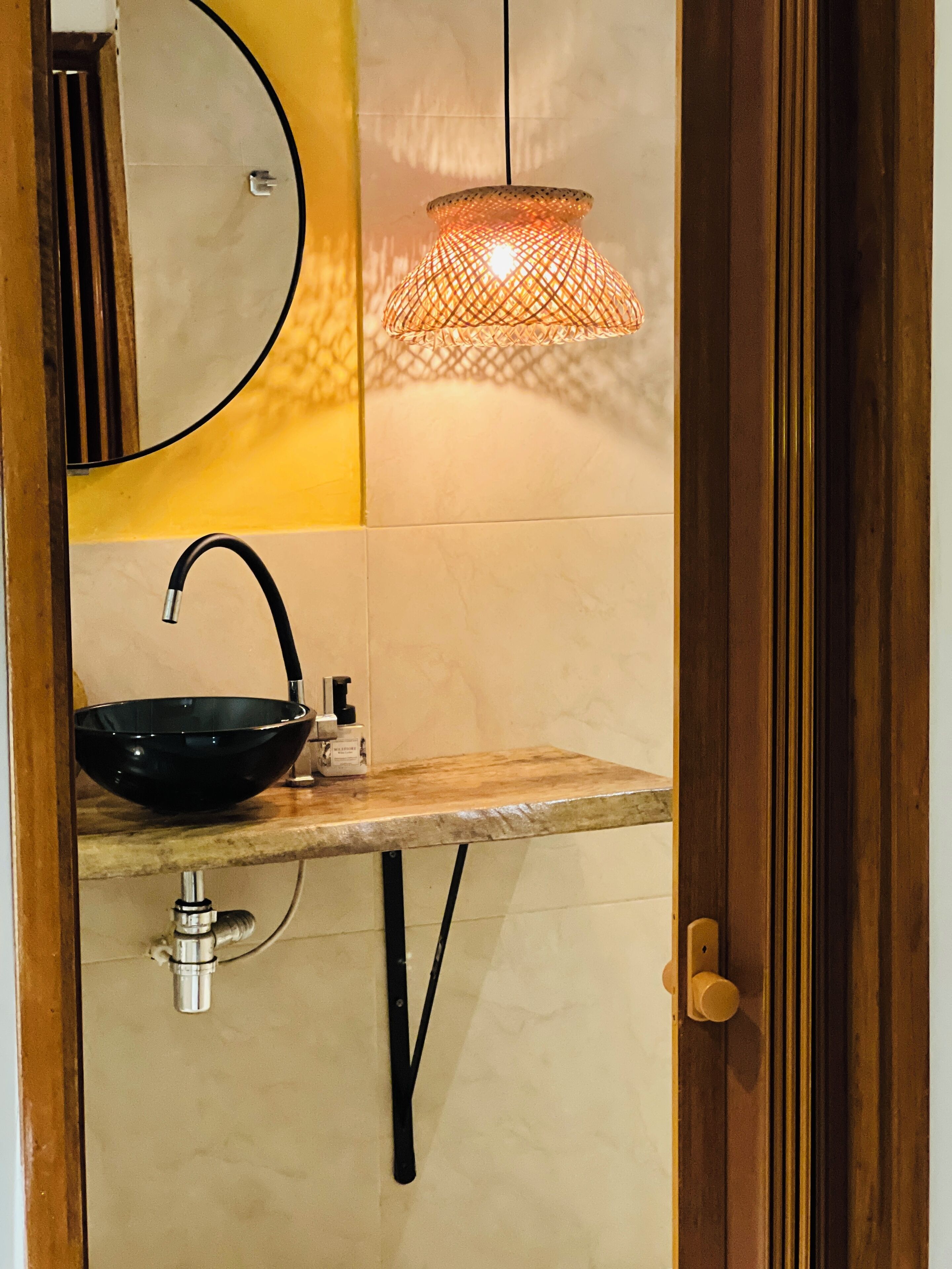 A bathroom with a round mirror, a black bowl sink, a wooden countertop, and a hanging lamp.