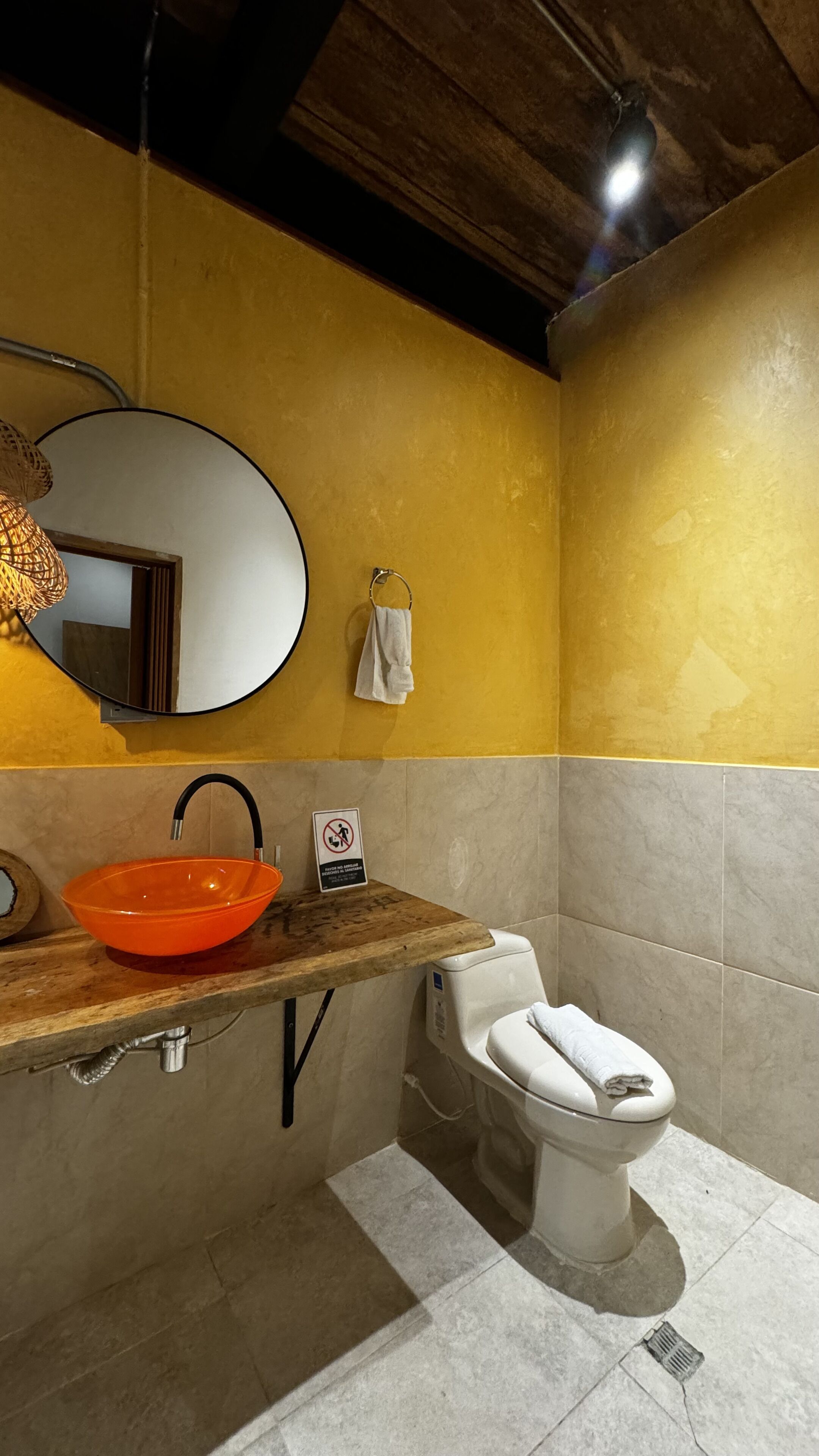 Een badkamer met een houten wastafelmeubel, een oranje wastafel, een wit toilet en een spiegel aan de muur.