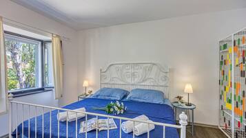 Ein Schlafzimmer mit einem Bett, zwei Nachttischen, einem Fenster mit Vorhängen, einer Wandverkleidung und Blick auf Bäume.