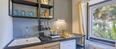 A compact kitchen with a sink, a built-in oven, and a window with a view of palm trees.