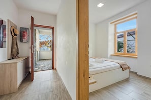 Ein Schlafzimmer mit Bett, Fenster, Tür und Schreibtisch mit Hut und Feuerlöscher.