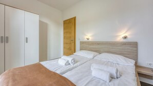 A modern bedroom with a large bed, two bedside tables, a wardrobe, and a wooden door.