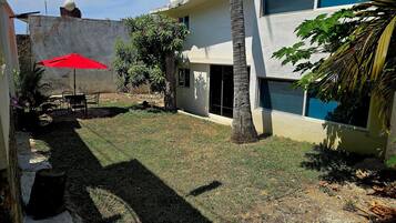 Un patio con una sombrilla roja, una palmera y un edificio con ventanales amplios.