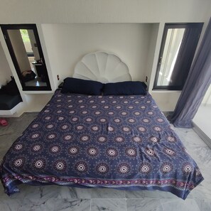 A bed with a patterned bedspread, a white headboard, and a view of a balcony through a window. - Secretos del Sol (Acapulco)