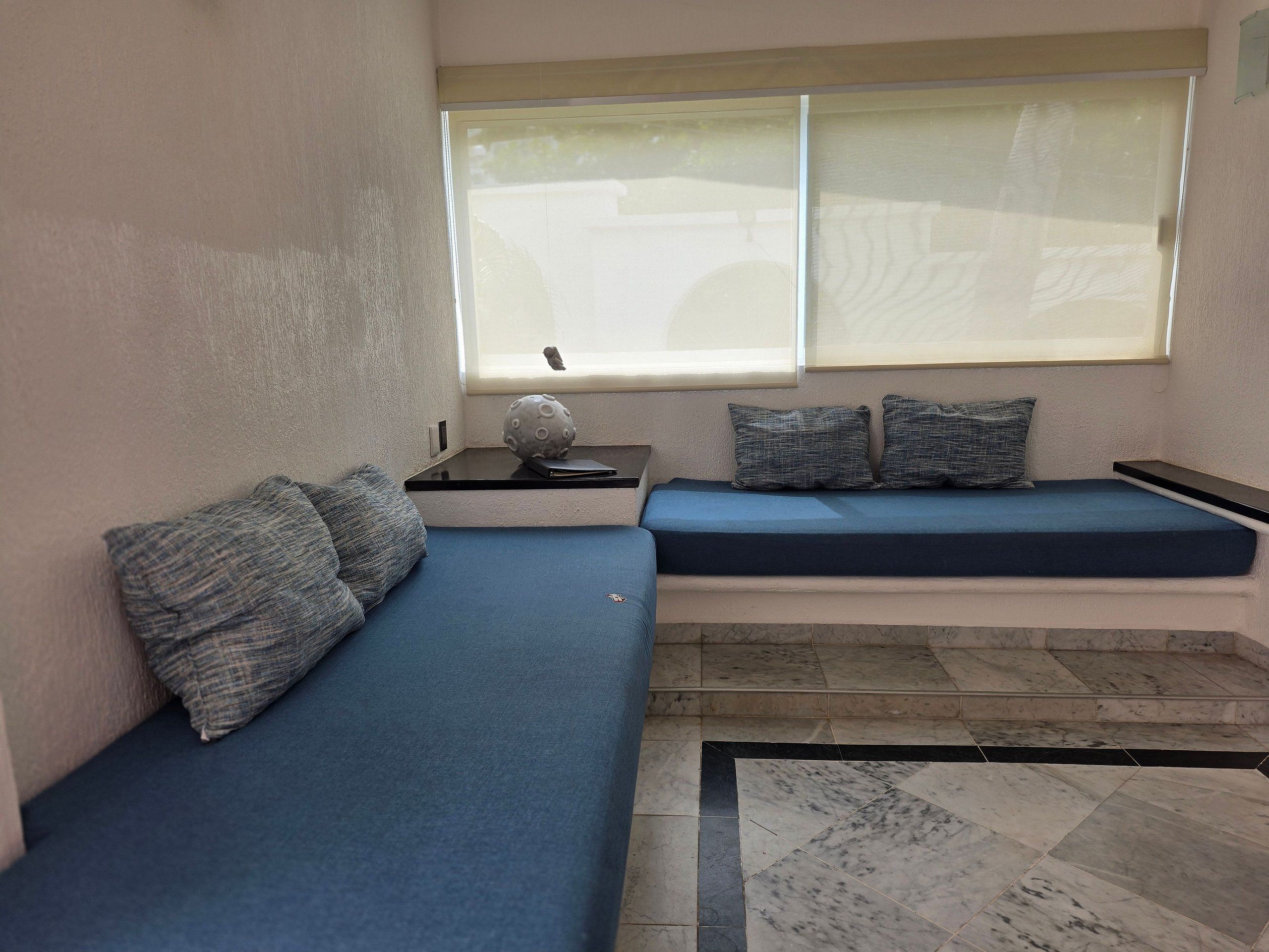 A room with a blue sofa, a small table with a globe, and a window with blinds.
