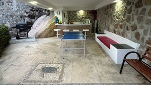 A room with a ping pong table, a bench, a small bar area, and a stone wall. - Secretos del Sol (Acapulco)
