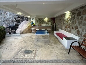 Una habitación con mesa de ping pong, banca, una pequeña zona de bar y una pared de piedra.