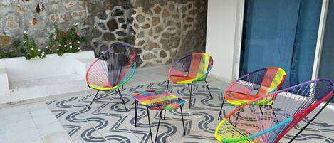 Un patio con quattro sedie colorate in filo metallico e un pavimento in piastrelle decorate.