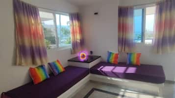 A room with two purple sofas, a small table with a neon light, and windows with colorful curtains.