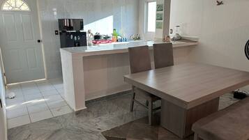 A modern kitchen with a central island, a dining area with a wooden table and chairs, and a white door with a window.