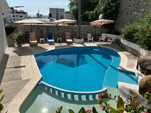 A swimming pool with lounge chairs and umbrellas, surrounded by stone walls and greenery. - Secretos del Sol (Acapulco)