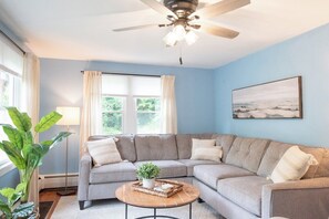 A living room with a sectional sofa, a ceiling fan, a floor lamp, and a window with curtains. - Bright Cottage Retreat in Central PA (Mcveytown)