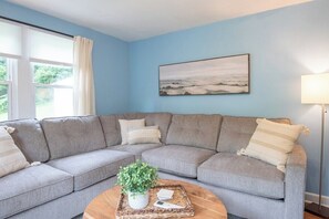 A living room with a grey sectional sofa, a coffee table with a plant, and a painting on the wall. - Bright Cottage Retreat in Central PA (Mcveytown)