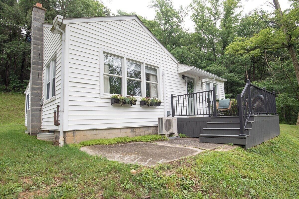 A white single-story house with a chimney, a front porch with a black railing, and a small staircase leading to the front door.